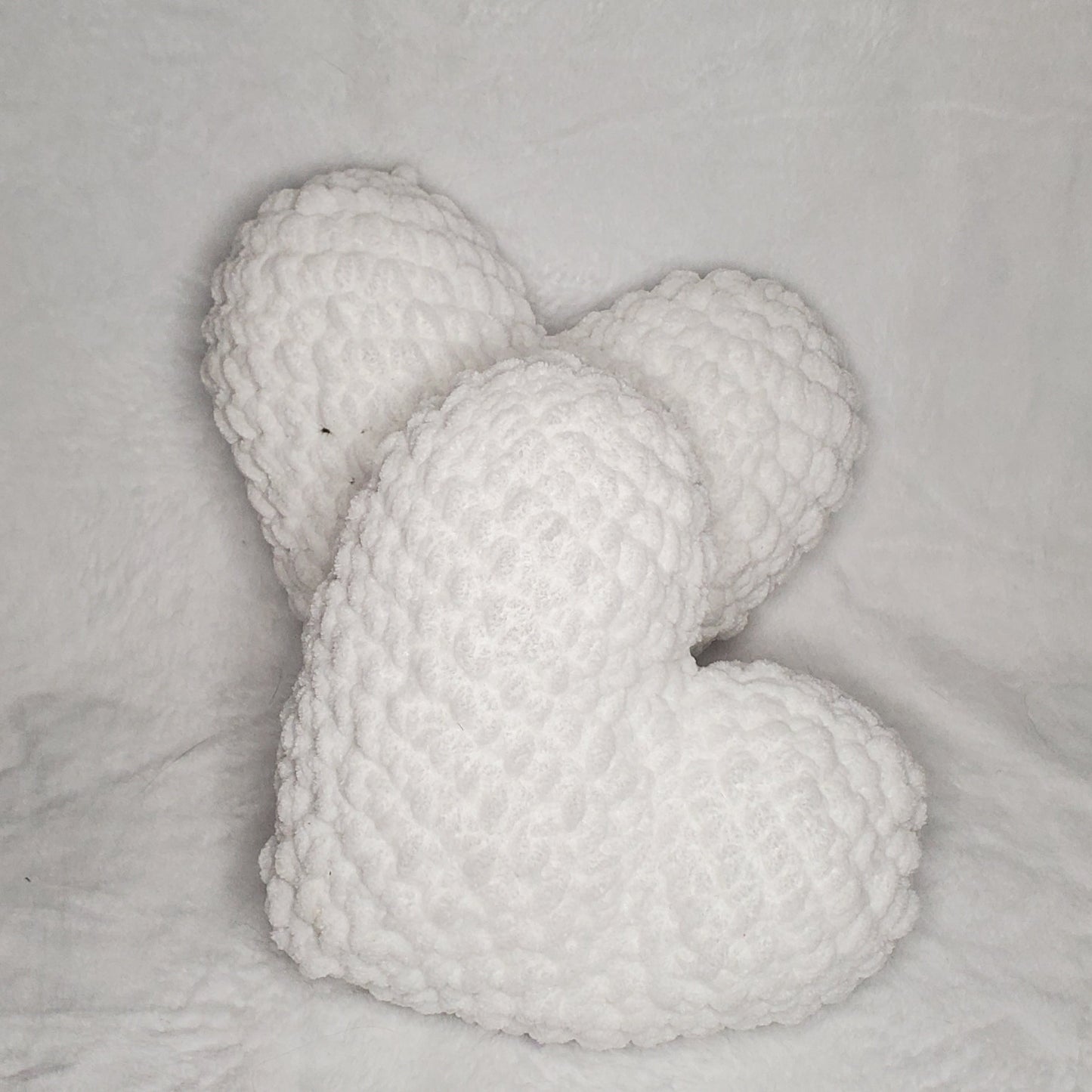 Two white knitted hearts on a textured gray surface